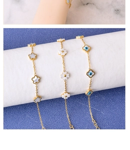 Detailed shot of gold bracelets featuring clover shell and blue evil eye charms on wrist