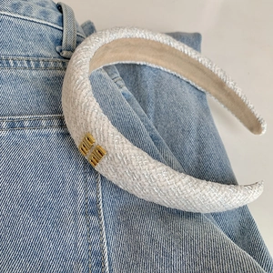 Cerchietto in tweed bianco stile francese con logo in metallo dorato su sfondo denim blu