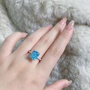 Macro shot of an emerald-cut aquamarine ring on a soft plush background with diamonds