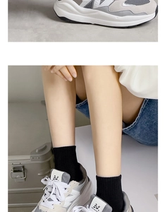 Dettaglio di sneaker grigie e bianche abbinate a calze nere classiche a metà polpaccio