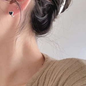 Close-up of small silver hoop earring featuring a black heart charm on a female model