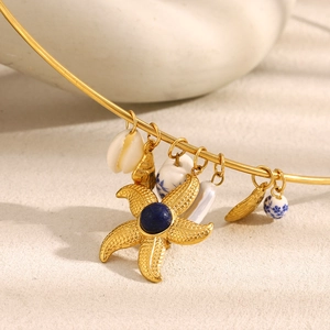 Macro detail of 18K gold-plated starfish pendant with blue gemstone on beach sand