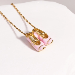 Detail of pink ballet shoe pendant with golden metal chain on white stone surface