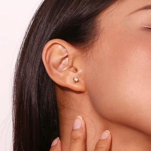 Close-up of a gold stud earring with a round clear zircon worn on a model's ear