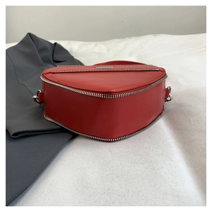 Detail of red heart-shaped shoulder bag with silver zipper on a white fabric background