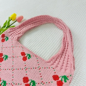 Detailed close-up of pink knit tote bag featuring red cherry and green leaf patterns