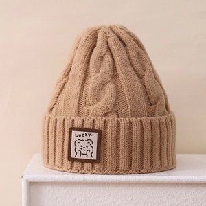Detail of chunky cable-knit winter hat featuring cute bear patch and ribbed cuff
