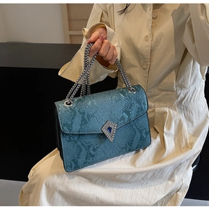 Detail showing the teal snakeskin texture and decorative gemstone buckle of the bag