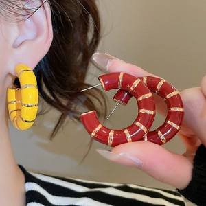 Close-up of yellow and red enamel C-shaped hoop earrings with gold striped accents