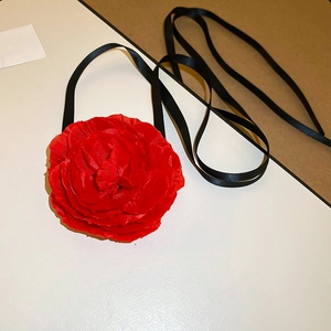 Detail of a large red fabric rose flower with a long black satin ribbon choker strap