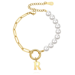 Detail of gold paperclip chain and white pearls bracelet with a letter R pendant