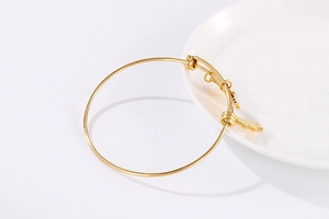 Detail of adjustable gold wire bangle with heart pendant on a white ceramic plate