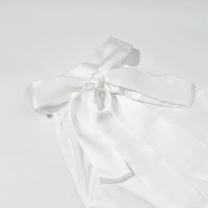 Close-up of white satin dress detailing a large elegant bow tie with silky luster