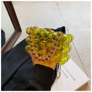 Detail of yellow acrylic hard shell bag with golden bead handle and fine chain strap