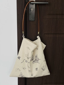 Detail of canvas bag featuring printed butterfly motif and brown leather handles