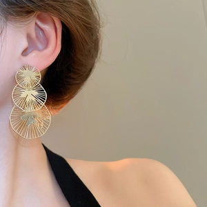 Détail de boucles d'oreilles dorées à pampilles étagées avec motif circulaire creux sur mannequin