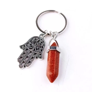 Macro detail of Hamsa Hand charm and hexagonal red goldstone crystal on a silver keychain