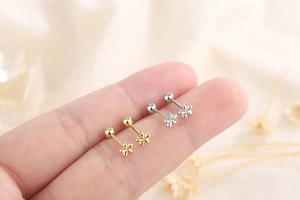 Macro view of tiny floral screw back earrings in gold and silver held by hand