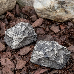 Detail of two realistic resin stone key hiders on wood mulch for garden security