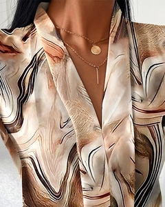 Detail of the V-neck sleeveless blouse with abstract earthy print and layered gold necklaces