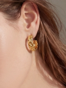 Close-up of golden C-shaped hoop earring with unique hammered texture on model