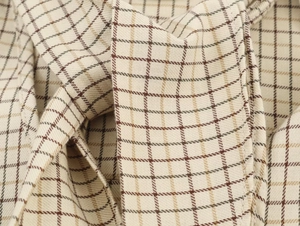 Close-up of the beige plaid cotton fabric texture with brown and green stripes on long sleeve shirt