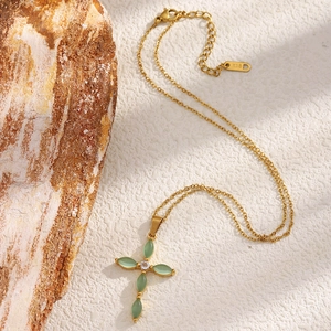 Collier croix plaqué or 18K avec pierres oeil-de-chat vertes sur fond de bois naturel