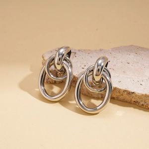 Macro detail of silver-tone interlocking geometric hoop earrings on a textured stone