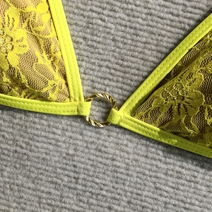 Detailed close-up of yellow floral lace bikini fabric with a golden metal ring connector