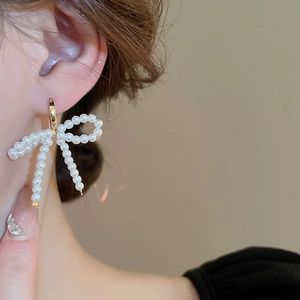 Gros plan de boucles d'oreilles nœud en perles élégantes portées avec créole dorée