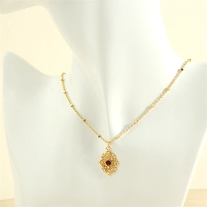 Detail of 18K gold necklace with red gemstone pendant and intricate filigree design