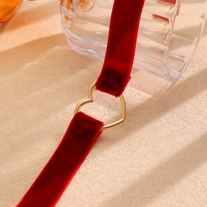 Dettaglio macro del girocollo in velluto rosso con anello a cuore in metallo dorato