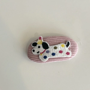 Cute pink knitted hair clip featuring an embroidered white dog with a yellow party hat