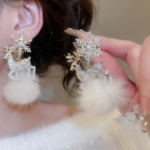 Close-up of reindeer and snowflake stud earrings with white fur balls on a model