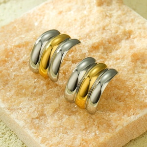 Macro detail of geometric C-shaped two-tone gold and silver earrings on stone base