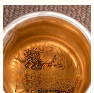 Macro top view of silver-plated tea cup with detailed dragon engraving and clear tea