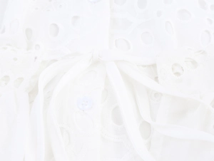 Detail shot of white shirt dress featuring a bow tie waist and round hollow embroidery