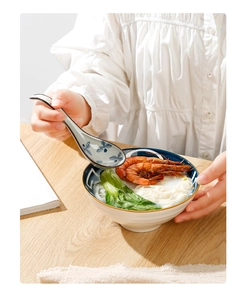 Macro shot of a long-handle ceramic spoon scooping noodles and shrimp in a blue bowl