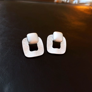 Macro detail of silver square earrings with textured finish on dark leather surface