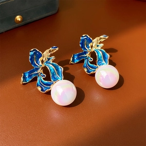 Detail of vintage iris flower earrings with blue enamel and large faux pearl on brown leather
