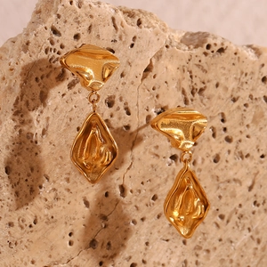 Detailed macro of 18K gold plated irregular geometric earrings on a beige stone surface