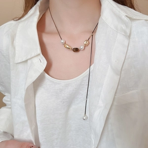 Detailed close-up of tiger eye and pearl floral pendant necklace on a linen shirt