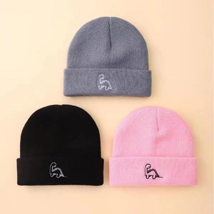 Close-up of three knit beanies in grey, black, and pink with dinosaur embroidery