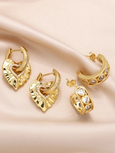 Detailed close-up of gold heart earrings set with zircon on luxury champagne silk