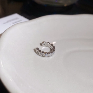 Detail of silver geometric ear cuff with zircon insets on a white ceramic tray