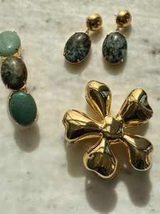 Detailed view of a gold flower shark clip and green stone jewelry on marble surface