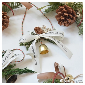 Close-up of Christmas pine cone ornament with golden bells and Best Wishes silk ribbon