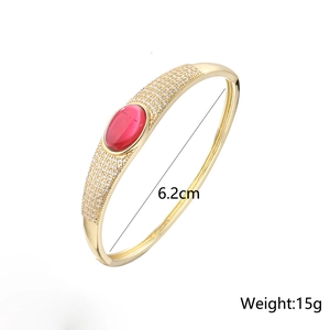 Detail view of gold-plated bangle showing red oval stone and white cubic zirconia stones