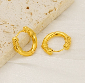 Gros plan sur des boucles d'oreilles dorées en acier titane avec motifs gravés rétro