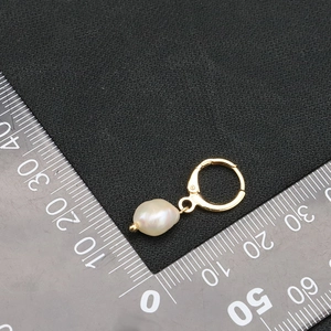 Single gold hoop earring with natural baroque pearl on black background with ruler